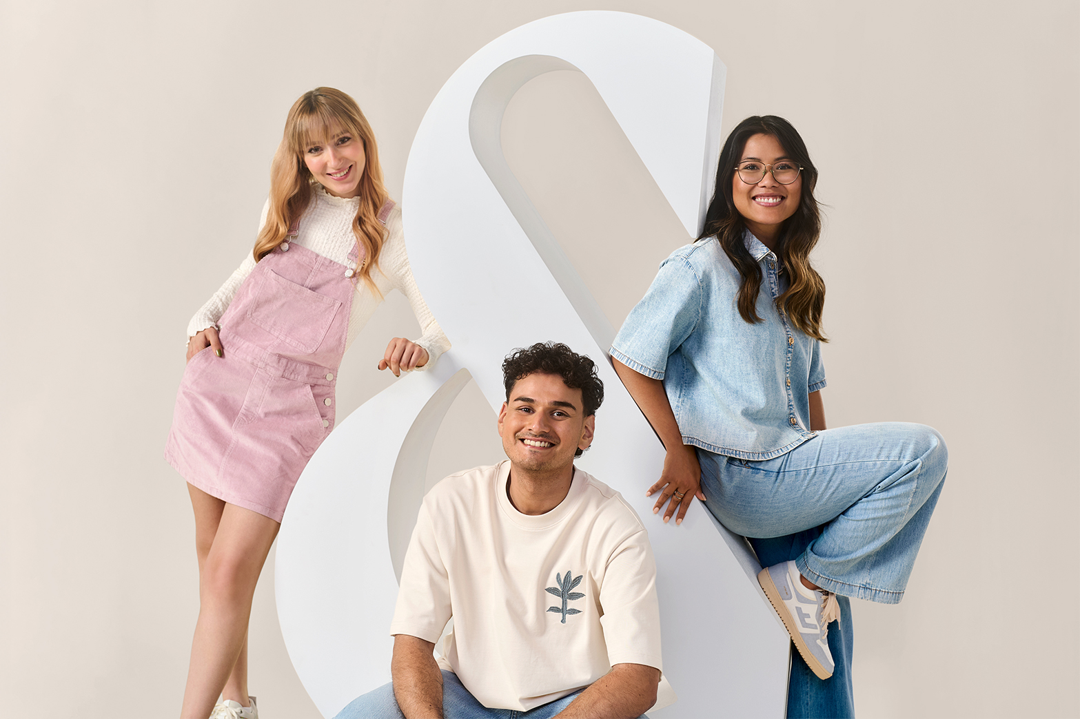 Zwei Frauen und ein Mann lehnen an ein physisches 3D Ampersand